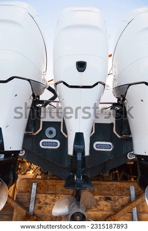 The stern of the boat, standing in a dry dock on supports with three outboard motors. Royalty-Free Stock Photo #2315187893