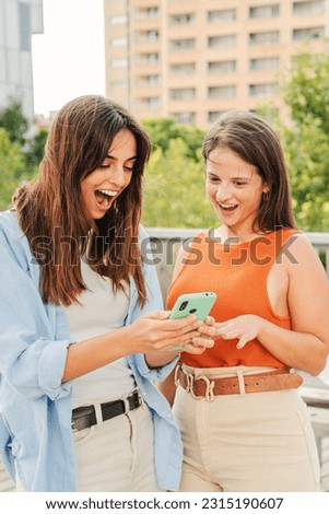 Vertical. Two cheerful smiling women watching and showing sale, news and social media on their smartphone app outside at the university campus. Young teenage females using a cellphone together. High