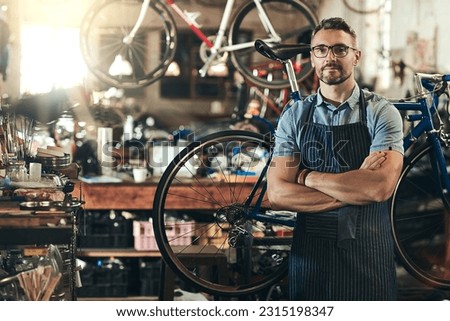 Portrait, serious and repair man in bicycle shop with arms crossed in workshop. Face, bike mechanic and confident male person, professional or mature technician and glasses in store or small business Royalty-Free Stock Photo #2315198347