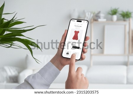 Woman shopping online with smart phone. Buying a red flow dress on ecommerce web page. Living room interior in background Royalty-Free Stock Photo #2315203575