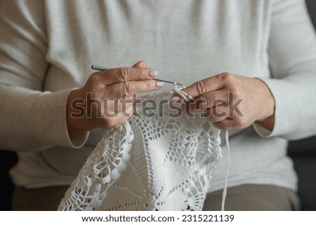 Old woman's hands knitting with crochet hook. Grandma crocheting with white thread a lace tablecloth. Handicraft concept