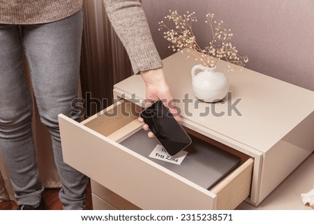 Close up of hand holding smartphone in separate desk drawer labeled Device Free Zone. Woman putting her phone in drawer with different gadgets at home. Digital detox and technology addiction concept Royalty-Free Stock Photo #2315238571