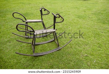 Two iron rocking horse sits on a path in the grass.