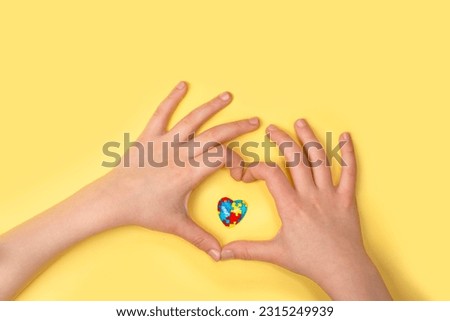 Autistic pride day - 18 june. World autism awareness day or month background. Child hands and jigsaw heart symbol on yellow background. Copy space Royalty-Free Stock Photo #2315249939