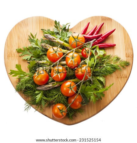 Fresh vegetables and herbs lie on a wooden board in a heart shape Isolated on white background