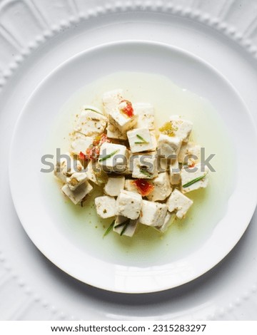 Top view of marinated feta cheese cubes on white plate. Cheese cubes marinating in herbed oil, flat lay of feta cheese in olive oil on plate