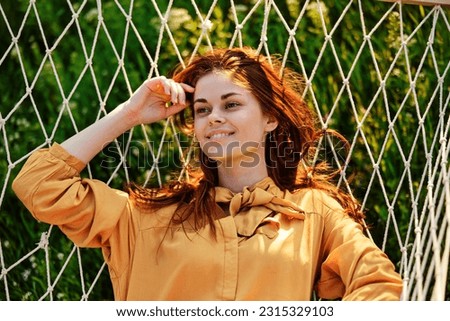 close horizontal photo of a beautiful, red-haired woman lying in a hammock enjoying a rest in an orange dress on a warm summer day
