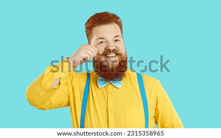 Headshot portrait of funny bearded redhead man isolated on blue studio background in suit with bow. Profile picture of smiling young red-haired man with mustache feel optimistic and overjoyed.