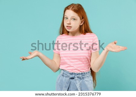 Little mistaken uncertain doubtful confused redhead kid girl 12-13 years old in pink striped t-shirt spread hands arms isolated on pastel blue background studio Children lifestyle childhood concept Royalty-Free Stock Photo #2315376779