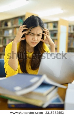 Exhausted female student sitting in library with laptop, suffering from headache or feeling tired of studying for college exam