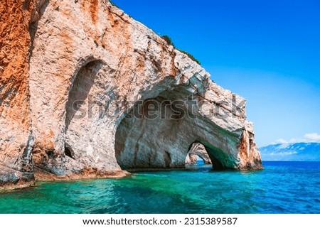 Zakynthos, Greece. Rock arches of Blue Caves from sightseeing boat with tourists in blue water of Ionian Sea. Greece holidays vacation tour with trip from Agios Nikolaos port. Royalty-Free Stock Photo #2315389587