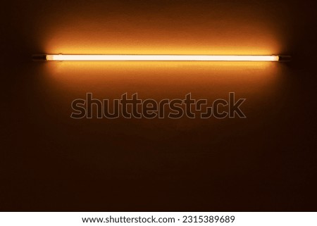 orange neon light bulb on white wall.	