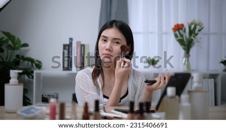Portrait of Beautiful young Asian woman blogger shows how to make up and use cosmetics at home. Business online, cosmetic and influencer marketing concepts.