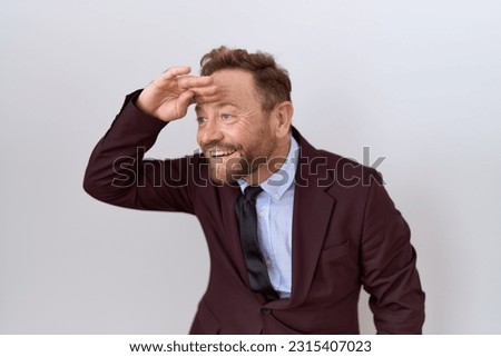 Middle age business man with beard wearing suit and tie very happy and smiling looking far away with hand over head. searching concept.  Royalty-Free Stock Photo #2315407023