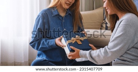 Closeup image of a young couple women giving and receiving a gift box to each other