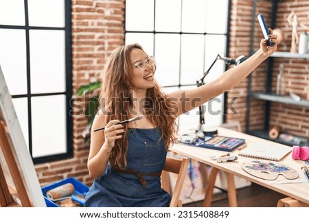 Young beautiful hispanic woman artist make selfie by smartphone at art studio