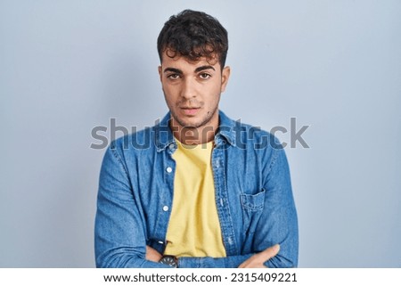 Young hispanic man standing over blue background looking sleepy and tired, exhausted for fatigue and hangover, lazy eyes in the morning. 