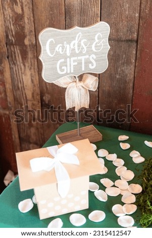 Decorative sign with words reading cards and gifts on a table with flower petals and a gift with a card wooden wall background