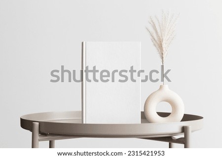 White book mockup with a reed pampas decoration on the beige table.