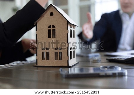 Agent and client discuss requirements for future apartment in agency office focus on wooden house model. Estate contract development