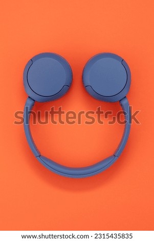 Blue wireless headphones on orange color background.  Headphones in the shape of a smile.