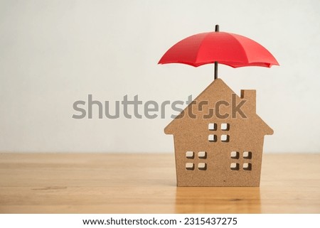Red umbrella cover home model on office wooden table with white wall background copy space. House, real estate, property insurance business, mortgage loan insurance concept. Insurance is risk control  Royalty-Free Stock Photo #2315437275