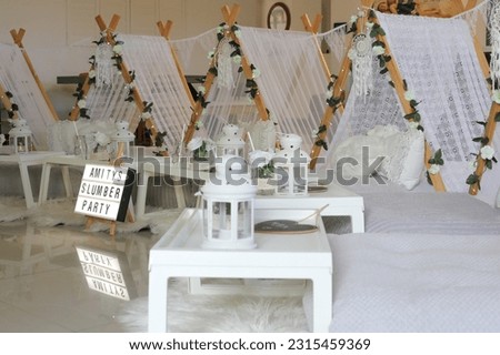 A boho themed girl's slumber party with white teepees, white lanterns, floral arrangement and white bedding.  Royalty-Free Stock Photo #2315459369