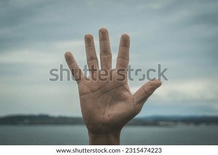gesturing with the hand, on an exterior background of sea and sky, five
