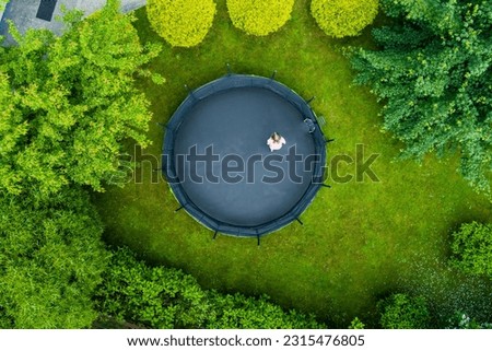 Aerial top-down view of a teenage girl jumping on a trampoline in a backyard. Backyard kids fun. Summer outdoor leisure activities. Royalty-Free Stock Photo #2315476805