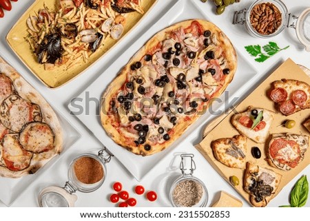 Photo from above of a table full of typical Italian food, pizza, pasta, and antipasti , on white table with ingredients 