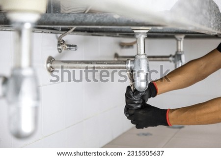 Technician plumber using a wrench to repair a water pipe under the sink. Concept of maintenance, fix water plumbing leaks, replace the kitchen sink drain, cleaning clogged pipes is dirty or rusty. Royalty-Free Stock Photo #2315505637