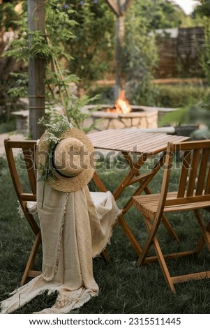 Wooden furniture in the garden against the backdrop of a fire on the patio. Among the branches of the bush stands a wooden table and chairs. 