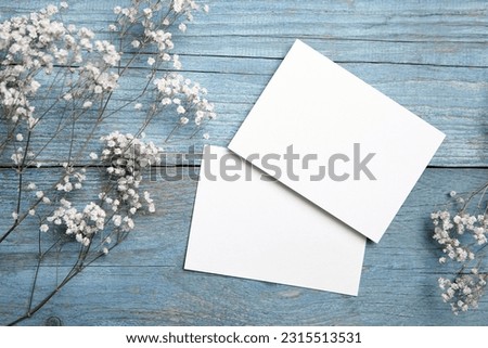 Card mockup, white blank wedding invitation with floral decor on bue wooden background. Greeting card mockup with white dried flowers on table