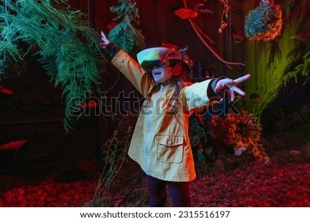 Little girl wearing luminous virtual reality headset standing near the trees. Augmented reality game in natural conditions. Concept of connection of the future technology and nature. Selective focus. Royalty-Free Stock Photo #2315516197