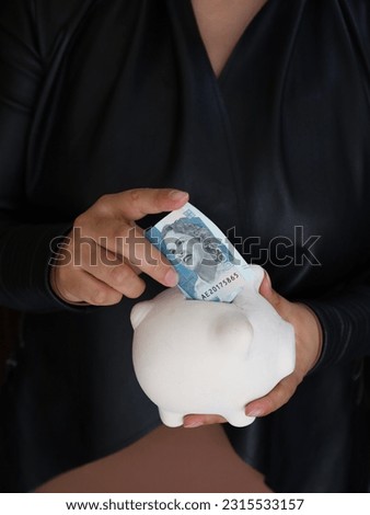 hands of a woman holding a Colombia banknote and a piggy bank