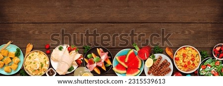 Summer food bottom border over a dark wood banner background. Assorted refreshing salads, fruit, wraps and BBQ grilled skewers. Top view. Copy space.