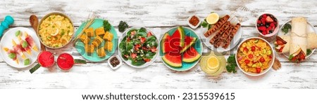 Summer food table scene over a white wood banner background. Mixture of refreshing salads, fruit, wraps and BBQ grilled skewers. Above view.