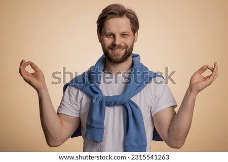 Keep calm down, relax, inner balance. Young caucasian man breathes deeply with mudra gesture, eyes closed, meditating with concentrated thoughts, peaceful mind. Guy isolated on beige background