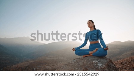  Asian woman wearing active wear do yoga practice meditating in mountains, lotus position. No stress, mindfulness, inner balance concept.Woman Yoga - relax in nature. Copy space.