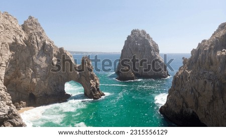 Arch of Cabo San Lucas aerial image during sunny summer day. Drone picture of rocky arch in Baja California Mexico. Turquoise green water and sharp rocky cliffs with blue skies in the background.