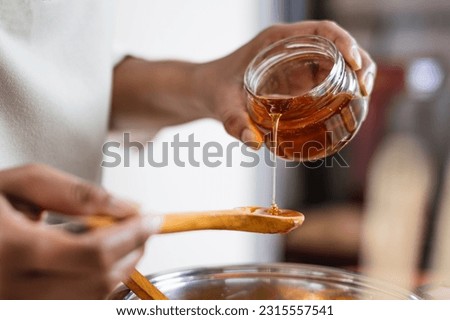 Female hands holding a bowl of bee honey and a wooden spoon. Close up. Elaboration of organic soap based on glycerin. Royalty-Free Stock Photo #2315557541