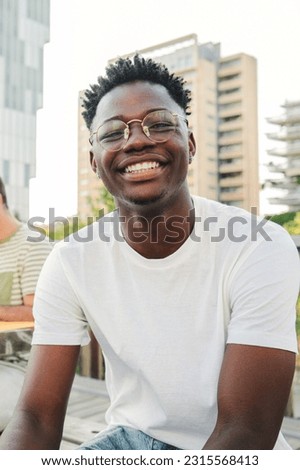 Vertical portrait of a smiling cheerful young African american student with a positive smile, white perfect teeth, looking at camera sitting outside taking a break at the university. High quality