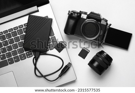 Laptop, external hard drive, modern digital camera with flip screen, two sd memory cards and lens on gray background. Photographer's equipment. Top view. Flat lay