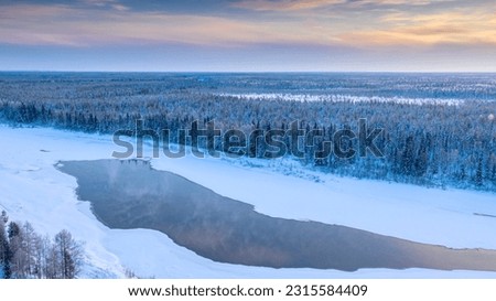 Steam rises above the ravine of the frozen river. Landscape of winter taiga. Russian winter of northern latitudes from a drone. Royalty-Free Stock Photo #2315584409
