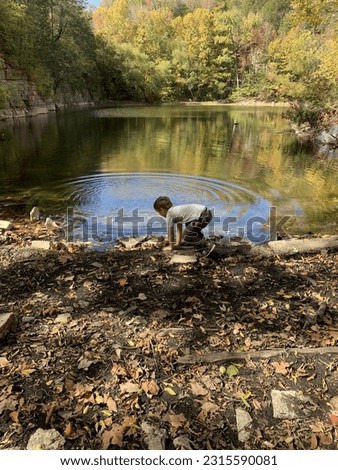 This is an image of a child that is on a hike and stopped to throw rocks in the pond.