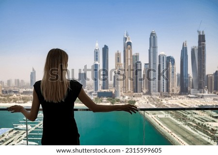 Rear view of young cute woman in black on balcony with view of skyscrapers Dubai UAE, pensive looking. Lovely lady posing from behind on terrace of tower block. Leisure activity concept. Copy ad space Royalty-Free Stock Photo #2315599605