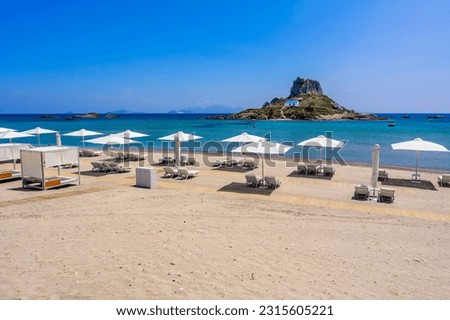 Deck chair and umbrella on beautiful Agios Stefanos Beach in front of paradise Island Kastri- historical ruins and paradise scenery at coast of island Kos, Greece Royalty-Free Stock Photo #2315605221