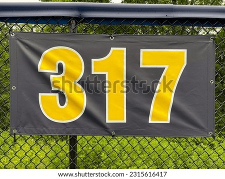 317 foot ft baseball field distance sign in yellow and black mounted on the black vinyl outfield fence.
