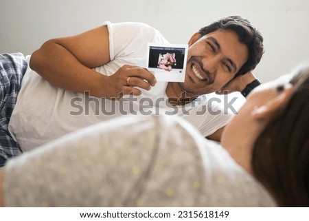 young husband holding a picture of his new baby while smiling with his wife, selective focus