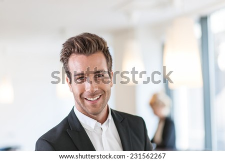 Portrait of a young businessman   standing at office, female colleague in the background